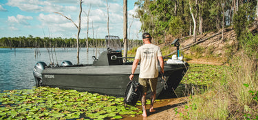 Man walking towards a boat on a lake with fishing equipment