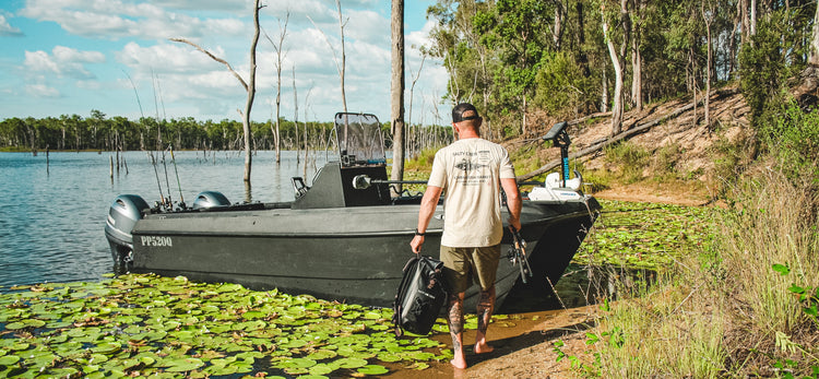 Man walking towards a boat on a lake with fishing equipment